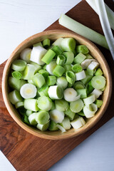 Chopped leeks in a wooden bowl on a white background.