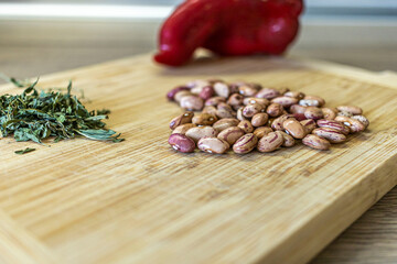 Closeup of a handful of kidney beans, dried spearmint and red pepper lied down on a wooden cutting board.
