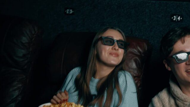 Couple in love A guy and a girl eat popcorn and watch a movie in a cinema using 3D glasses. Concept of a movie show in a cinema