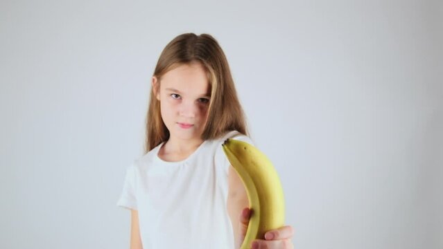 Close-up preteen girl enjoying healthy food. Portrait little girl in her 7 holding delicious banana with white isolated background