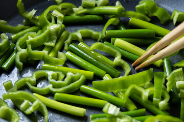 ピーマンとにんにくの芽をフライパンで炒める調理シーン。
