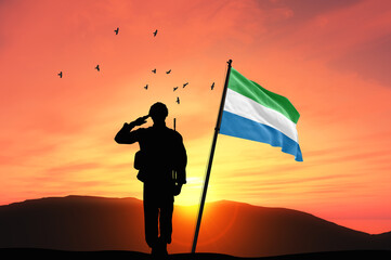 Silhouette of a soldier with the Sierra Leone flag stands against the background of a sunset or...