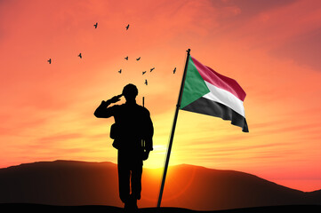 Silhouette of a soldier with the Sudan flag stands against the background of a sunset or sunrise....