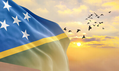 Waving flag of Solomon Islands against the background of a sunset or sunrise. Solomon Islands flag for Independence Day. The symbol of the state on wavy fabric.