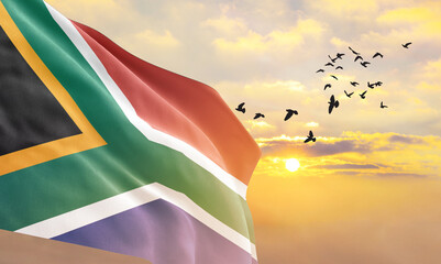 Waving flag of South Africa against the background of a sunset or sunrise. South Africa flag for...