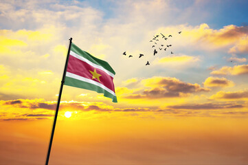 Waving flag of Suriname against the background of a sunset or sunrise. Suriname flag for Independence Day. The symbol of the state on wavy fabric.