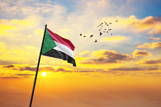 Waving flag of Sudan against the background of a sunset or sunrise. Sudan flag for Independence Day. The symbol of the state on wavy fabric.