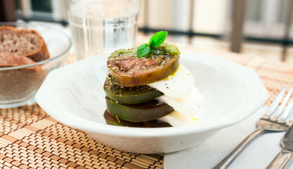 Caprese salad with mozzarella, black tomatoes and pesto in white plate