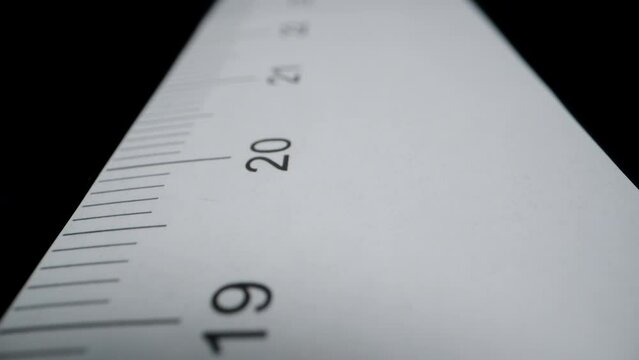 Paper ruler on a black background, with centimeter measurements. Dolly slider extreme close-up.