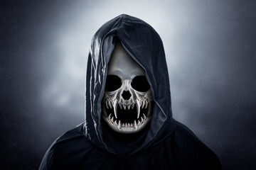Grim reaper in hooded cloak over dark misty background at night