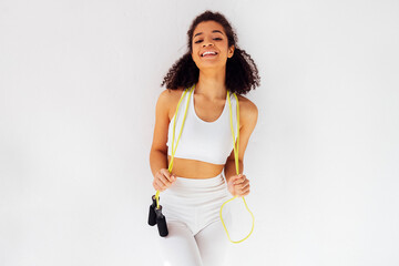 Slim young afro woman in white top and leggings with jump rope on her neck