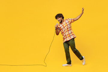 Full body young singer Indian man he wear shirt casual clothes sing song in microphone at karaoke club raise up hand isolated on plain yellow color wall background studio portrait. Lifestyle concept. - obrazy, fototapety, plakaty