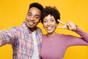 Close up young couple two friend family man woman of African American ethnicity in casual clothes together do selfie shot pov mobile cell phone show v-sign isolated on plain yellow orange background