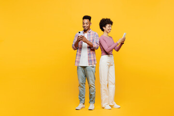 Full body smiling fun young couple two friend family man woman of African American ethnicity wear purple casual clothes together hold in hand use mobile cell phone isolated on plain yellow background