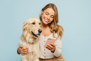 Young fun owner woman with her best friend retriever wear casual clothes hold mobile cell phone use internet hug dog isolated on plain pastel light blue background studio. Take care about pet concept.