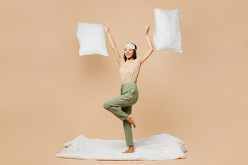 Full body excited happy young calm Latin woman she wear pyjamas jam sleep eye mask rest relax at home dance with pillow on duvet isolated on plain pastel beige background. Good mood night nap concept