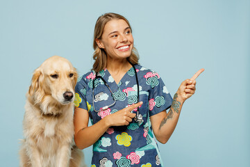 Young veterinarian woman she wears uniform stethoscope heal exam hug cuddle embrace retriever dog point finger aside on area isolated on plain pastel blue background studio. Pet health care concept.