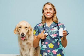 Young smiling veterinarian woman wear uniform stethoscope heal exam retriever dog hold point on container with pills treatment isolated on plain pastel blue background studio. Pet health care concept.