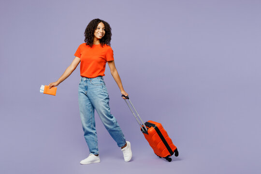 Traveler kid teen girl she wear orange t-shirt hold bag passport ticket look aside isolated on plain purple background. Tourist travel abroad in free time rest getaway Air flight trip journey concept