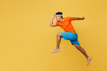 Fototapeta na wymiar Full body side profile view young fitness trainer sporty man sportsman wear orange t-shirt jump high run fast spend time in home gym isolated on plain yellow background. Workout sport fit abs concept.