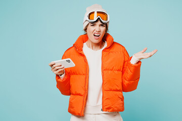 Skier sad young woman wear padded windbreaker jacket hat ski goggles mask play racing app on mobile cell phone travel rest spend weekend winter season in mountains isolated on plain blue background.