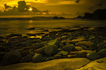 Sunset at the rocky beach in Papuma, Jember, East Java, Indonesia. Cloudy afternoon with ocean...