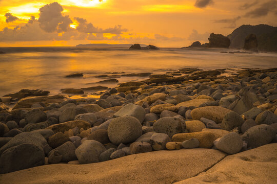 Sunset at the rocky beach in Papuma, Jember, East Java, Indonesia. Cloudy afternoon with ocean waves swipe the sands. Nature and Landscape Photography.