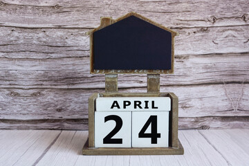 Chalkboard with April 24 date on white cube block on wooden table.