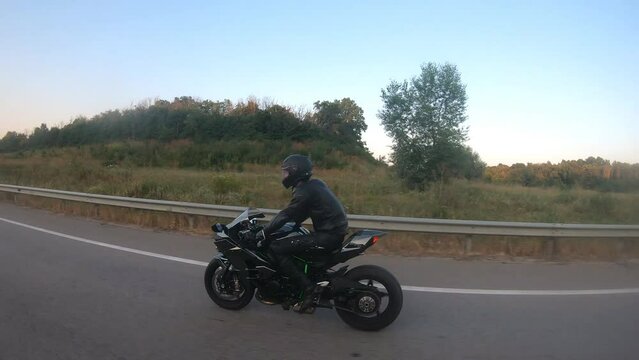 Motorcyclist racing his motorcycle on country road. Guy driving bike during trip. Young man in helmet riding fast on modern sport motorbike at highway. Side view Close up Slow motion