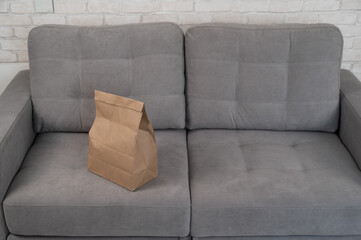 Kraft paper bag with food delivery on gray sofa. 