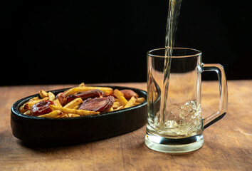 foam in a glass with beer and fried sausages with potatoes on a wooden background.Oktoberfest.