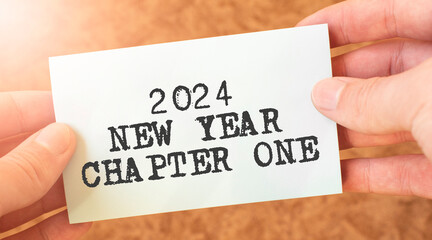 2024 NEW YEAR CHAPTER ONE word inscription on white card paper sheet in hands of a businessman.