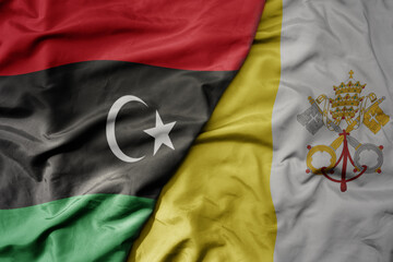 big waving national colorful flag of vatican city and national flag of libya .