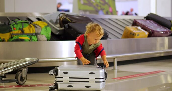 Little boy is trying to lift suitcase lying on floor. Small trolley case is probably not very heavy, but it is still quite challenging for young passenger. Young child manages to lift it
