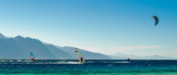 windsurfers and kitesurfers ride in the Red Sea on the background of the rocky coast in Egypt Dahab...