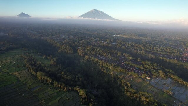 Scenic aerial shot of Balinese landscape with Agung mountain on background, evening time. Camera gracefully soar towards Bangli area, green ravines and rice fields, some small villages seen down