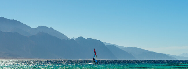 windsurfer rides in the Red Sea against the backdrop of high rocky mountains in Egypt Dahab