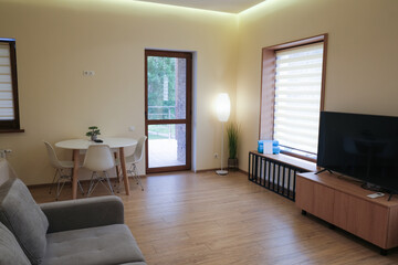 Modern design of a living room in a hotel. Chair, bed, table, TV. Exit to a balcony with a transparent glass door.