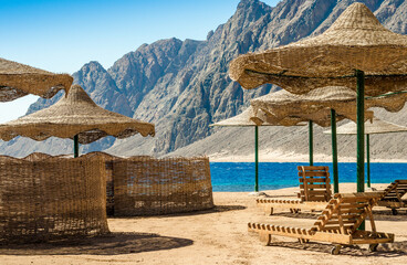 beach umbrellas and wooden lounge chairs on the sand of the beach against the backdrop of the sea...