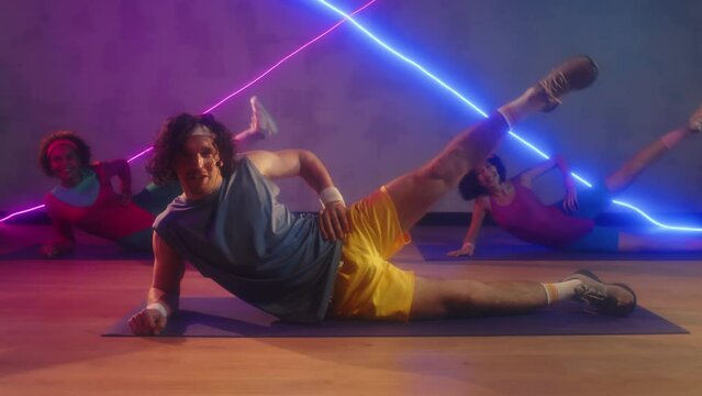 Male coach and two biracial sportswomen doing side leg raises on floor in retro outfits