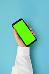 Hand in a white shirt holding a phone with a green screen on a blue background
