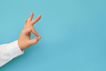 A hand in a white shirt shows the Ok gesture on a blue background