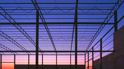 Obraz premium Silhouette of metal roof beam and column of industrial factory building outline structure in construction area against colorful twilight sky background