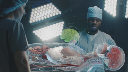 Diverse surgeons work in operating room. African American doctor talks with colleague, uses virtual holographic display with 3D graphics of human skeleton and organs. AR in medicine. Advanced surgery.