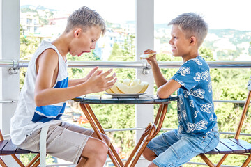 Preteen and junior schoolboys enjoy eating fresh melon on hotel terrace. Brother siblings eating...