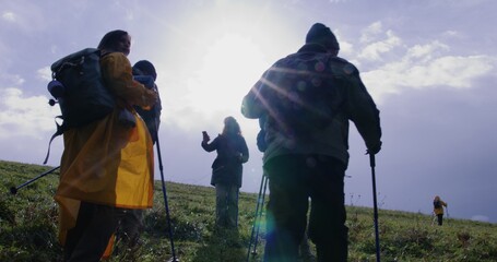 Following shot of travelers group with trekking poles walking along trail on beautiful hill. Tourists discover amazing nature beauty. Tourism and outdoor exploration. Slow motion. Feet close up.