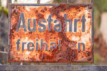old rusty sign Ausfahrt freihalten, english keep way, at an old gate