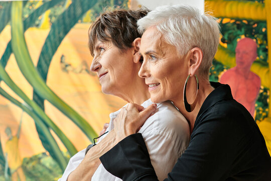 side view of trendy and smiling lesbian mature artists looking away in contemporary art workshop