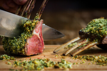 Rack of lamb with hazelnut herb crust being cut with large knife on wooden board in restaurant