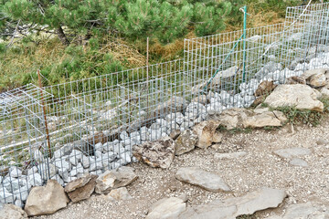 Gabion building process. Unfinished gabion building of rocks and metal mesh in nature park. Filling steel net basket with stones to make fence in garden. Border construction site